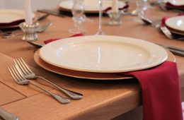 A wooden table with gold charger plates and white crockery, with red table linen and glass candlesticks