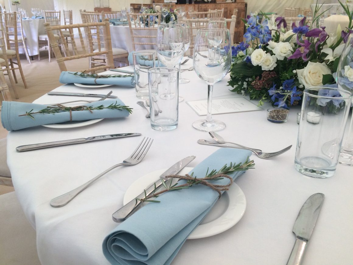 Wide rustic wooden trestle tables with botanical theme, white pillar candles and ivory crockery