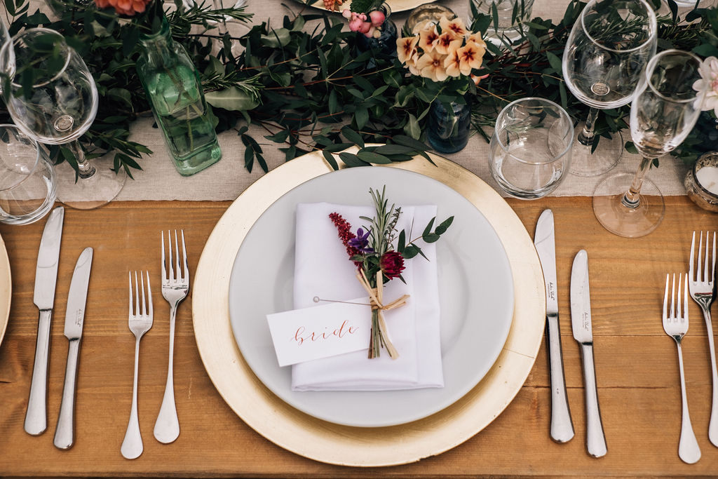 Wide rustic wooden trestle tables with botanical theme, white pillar candles and ivory crockery
