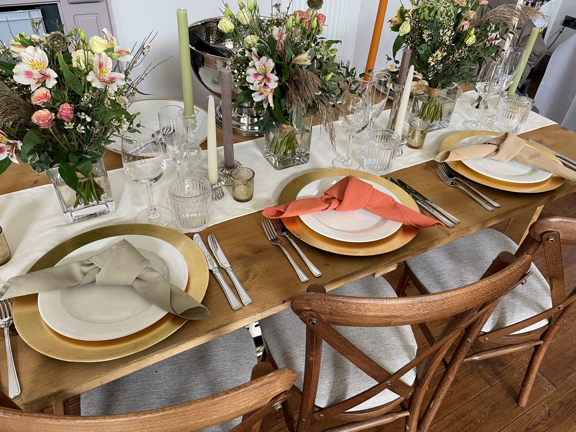 Wide rustic wooden trestle tables with botanical theme, white pillar candles and ivory crockery